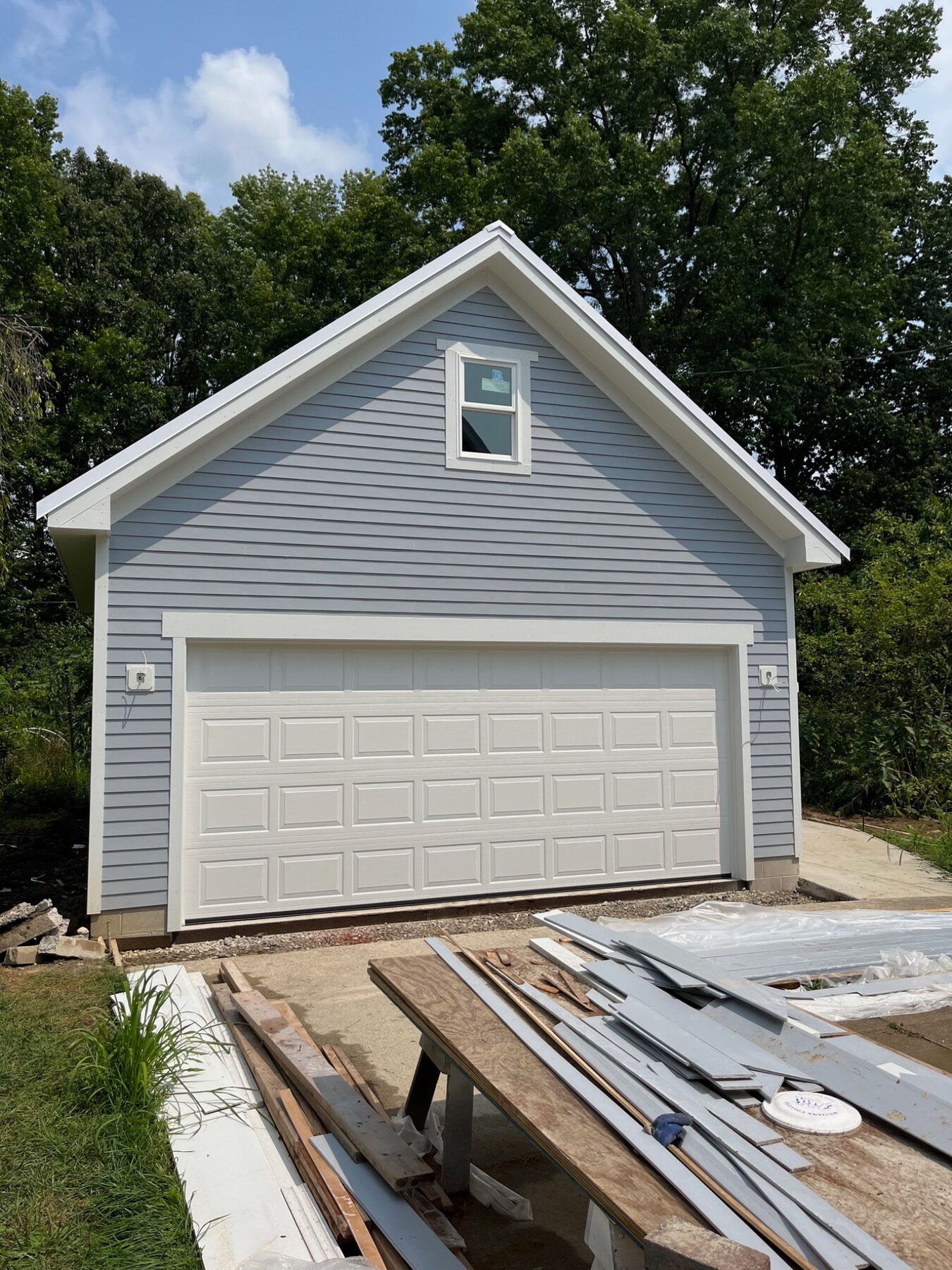 New garage finished with gray vinyl siding, white trim and a metal roof
