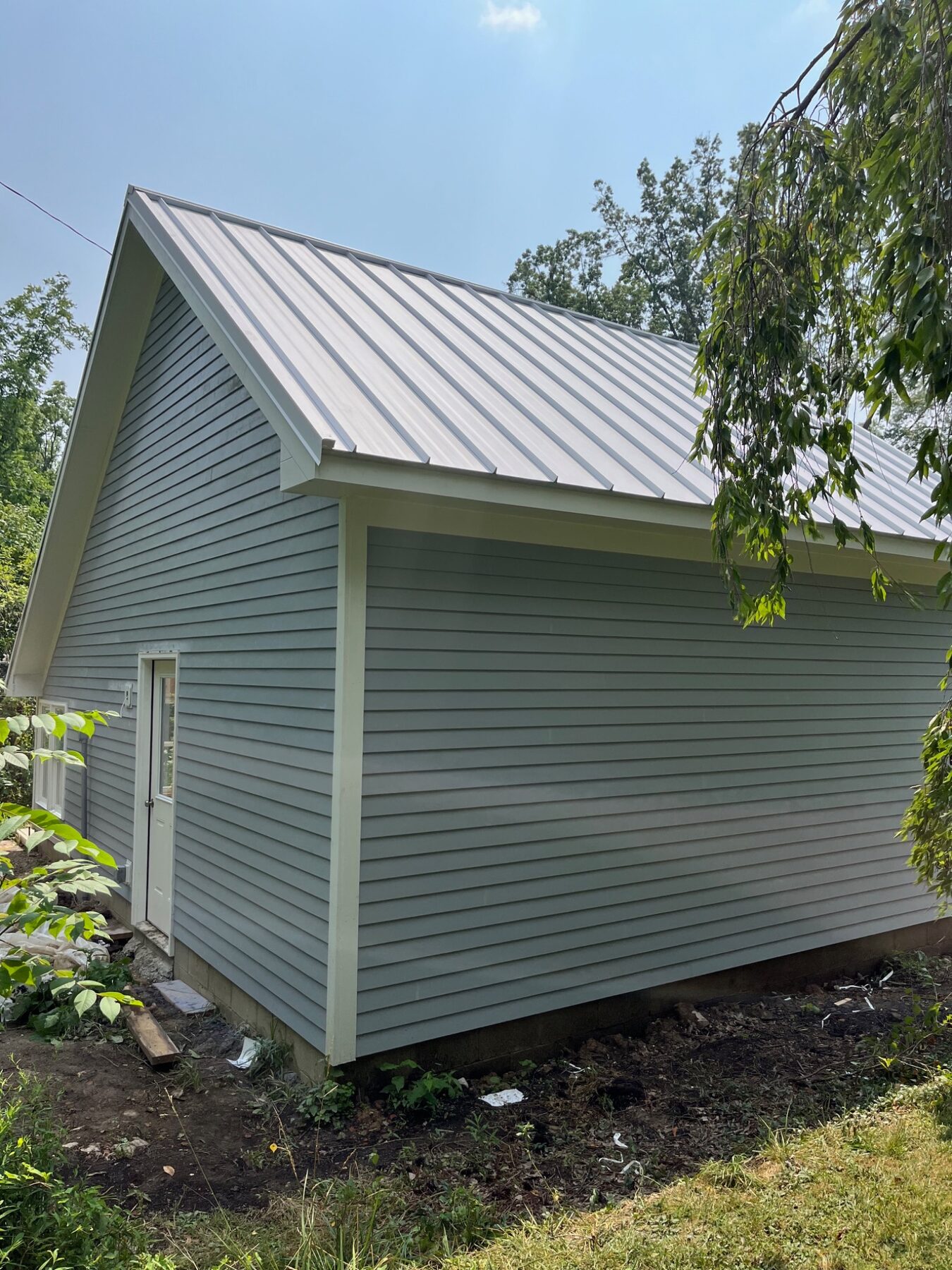 Side view of a garage finished with gray siding, white trim and a metal roof